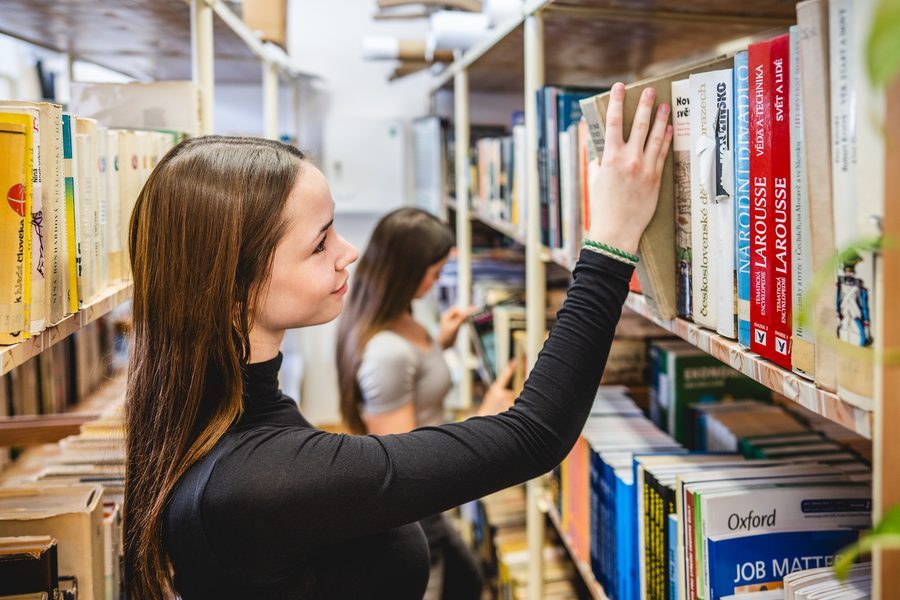 Studentky vybírají knihu ve školní knihovně
